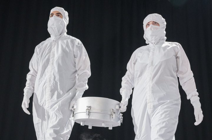 Two NASA personnel carry a container holding the sample gathered from the Bennu asteroid.