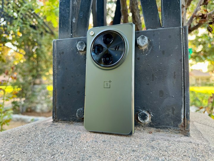 OnePlus Open in Emerald Dusk leaning against pole.