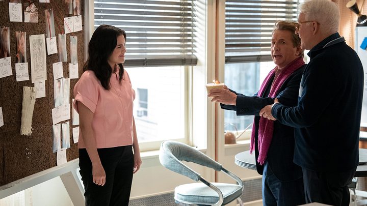 Oliver and Charles offering Mabel a cupcake with a candle in it, their murder board behind them in a scene from Only Murders in the Building season 3.