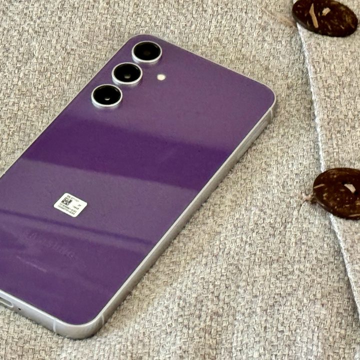 A Samsung Galaxy S23 FE in purple, showing its back, sitting on a pillow.