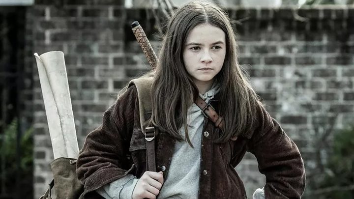 Judith from The Walking Dead walking with a backpack and weapons.