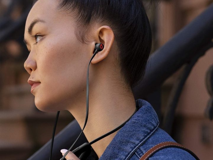 A woman adjusts the volume on her Beats Flex wireless earbuds.