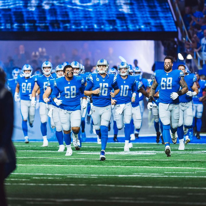The Detroit Lion football players run out of the tunnel on a field.