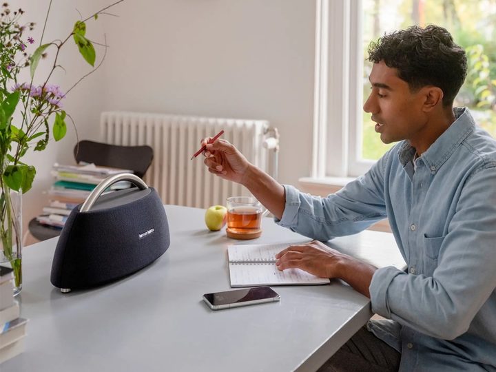 A man works at a table next to the Harmon Kardon Go+Play Bluetooth speaker.
