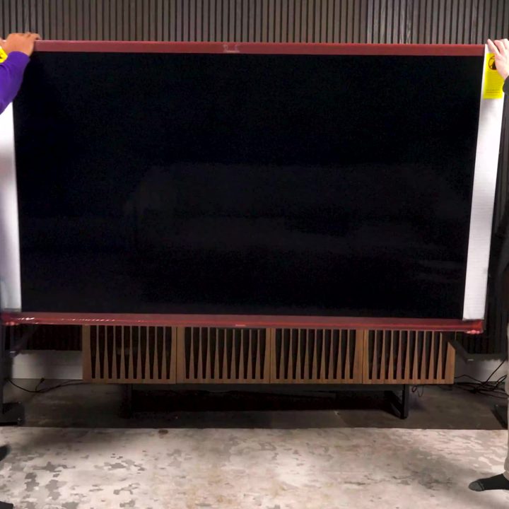 Two men lift a Hisense UX TV onto a media console.