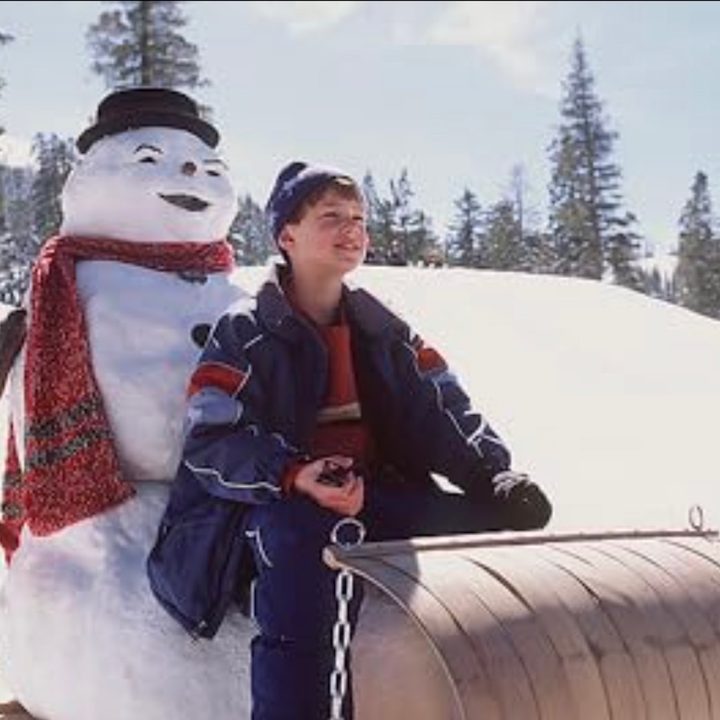 A boy goes down a hill on a sled with a snowman.