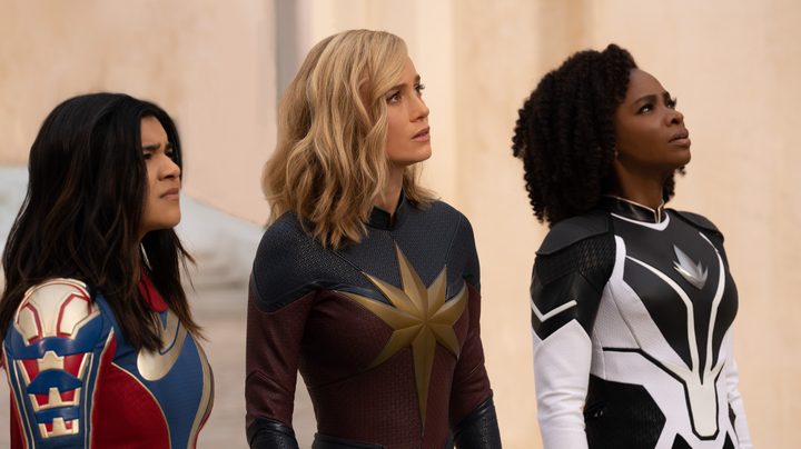 Iman Vellani, Brie Larson, and Teyonah Parris look offscreen at something.