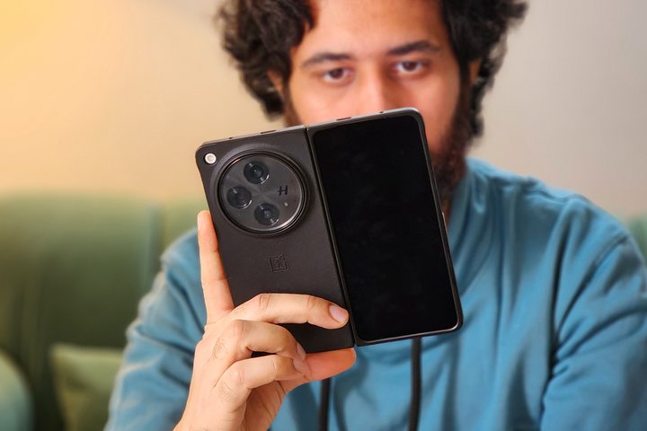 OnePlus Open black color held in hand and being used by a man wearing a blue hoodie.