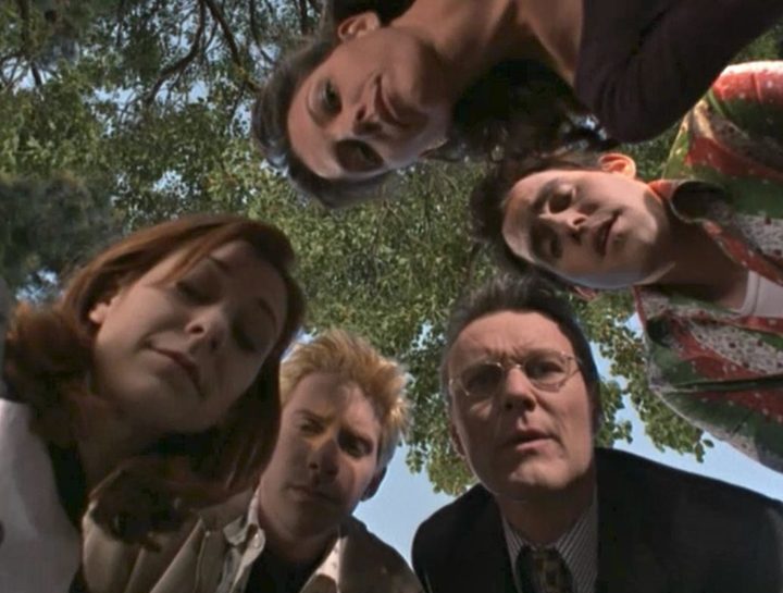 Willow, Cordelia, Xander, Giles, and Oz stand in a circle, looking down at the camera, concerned.