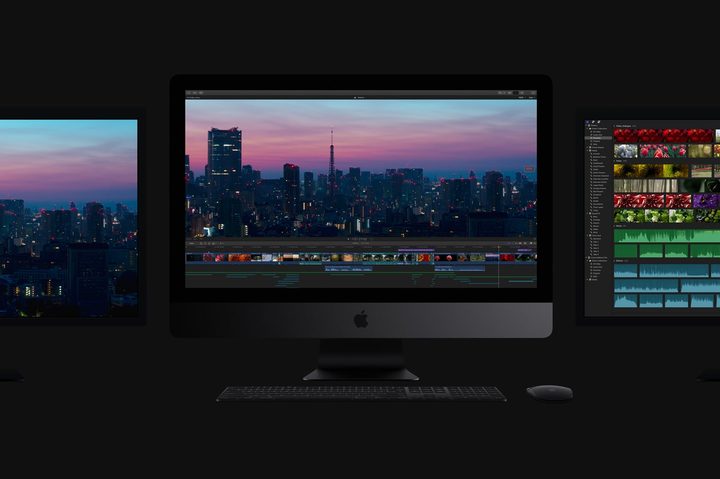 An Apple iMac Pro in a dark room flanked by two monitors, one on either side of it.