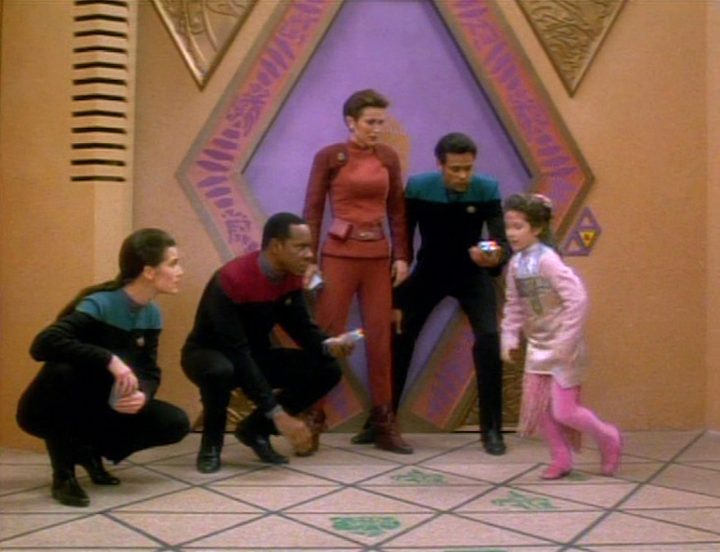 Jadzia Dax, Ben Sisko, Kira Nerys, and Julian Bashir watch a young girl play hopscotch in the DS9 episode "Move Along Home"