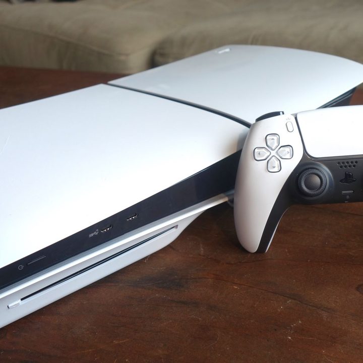 A PS5 sits on a table with a DualSense standing up next to it