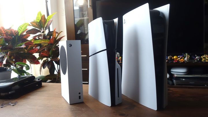 An Xbox Series S, 2023 PS5, and 2020 PS5 stand in a line.