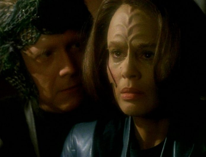 B'Elanna Torres looks tearfully offscreen while a man stares over her shoulder in the Voyager episode "Remember"