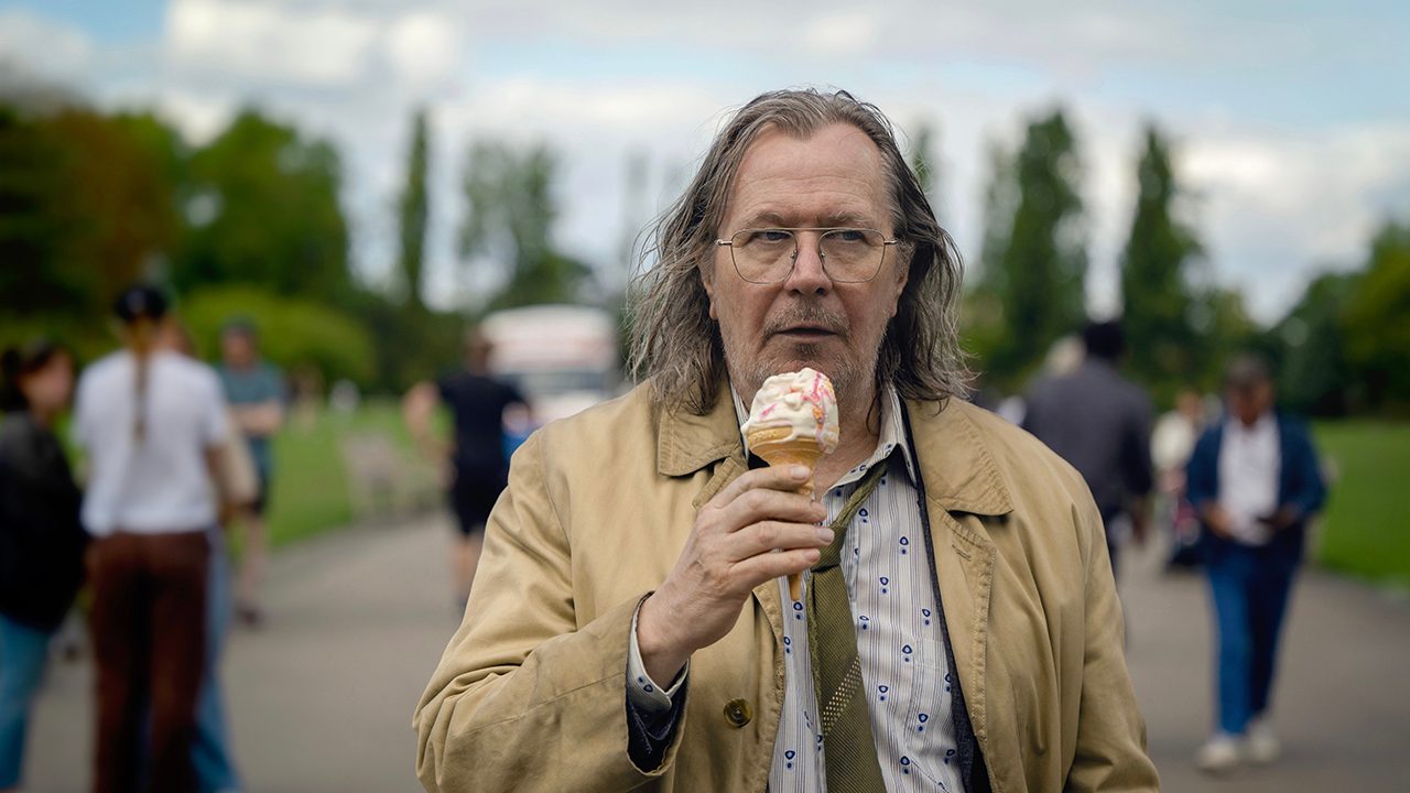 Gary Oldman in Slow Horses season 3 on Apple TV+, walking down the street eating ice cream.