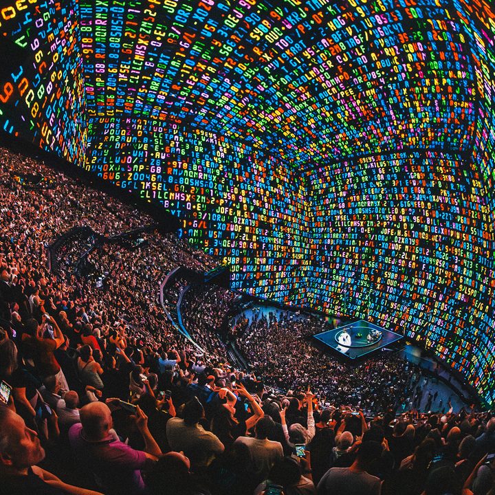 An image showing the audience and the band U2 as the wraparound visualization of letters and numbers seems to skew perspective inside the Sphere in Las Vegas.