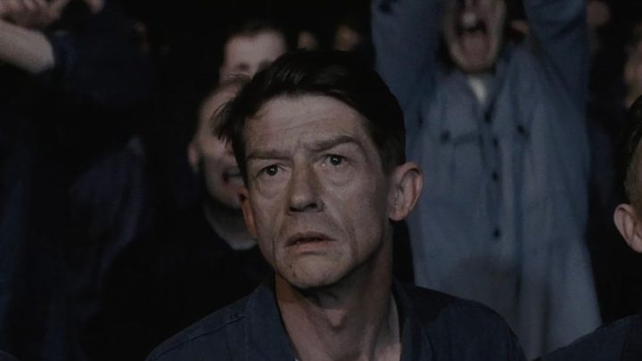 A man stares up from a crowd looking terrified in a scene from 1984.