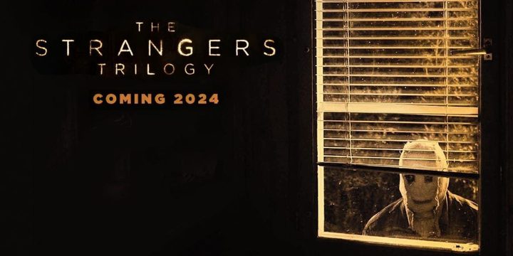 A masked man looks through a window in The Strangers