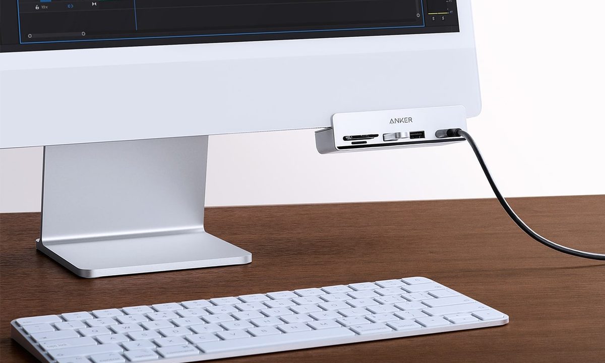 The Anker 535 USB-C Hub attached to the underside of an Apple iMac. There is an Apple Magic Keyboard on the desk in front of the iMac.