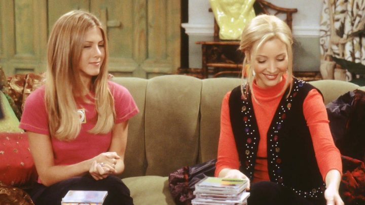 Rachel and Phoebe smiling while sitting on a couch in Phoebe's apartment in Friends.
