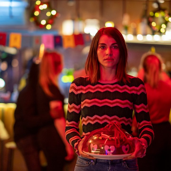 A woman holds a cake and walks toward the camera.