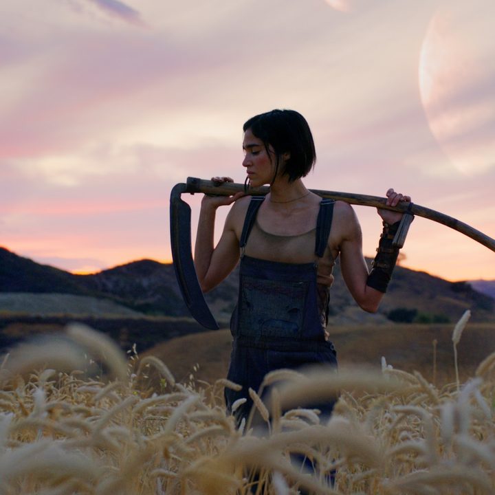 Sofia Boutella strikes a cool pose with a stick against a pretty landscape in a still from Rebel Moon – Part One: A Child of Fire.