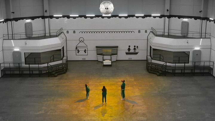 Three people stand in an empty room in Squid Game: The Challenge.