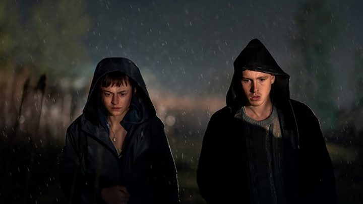 Darby and Bill walking outside in the cold, both with black hoodies in a scene from A Murder at the End of the World.