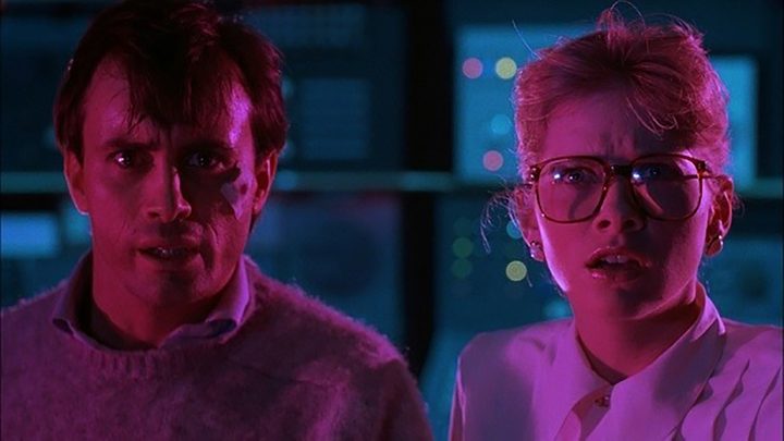 A man and a woman in a dark lab with light on them staring stunned in a scene from From Beyond.