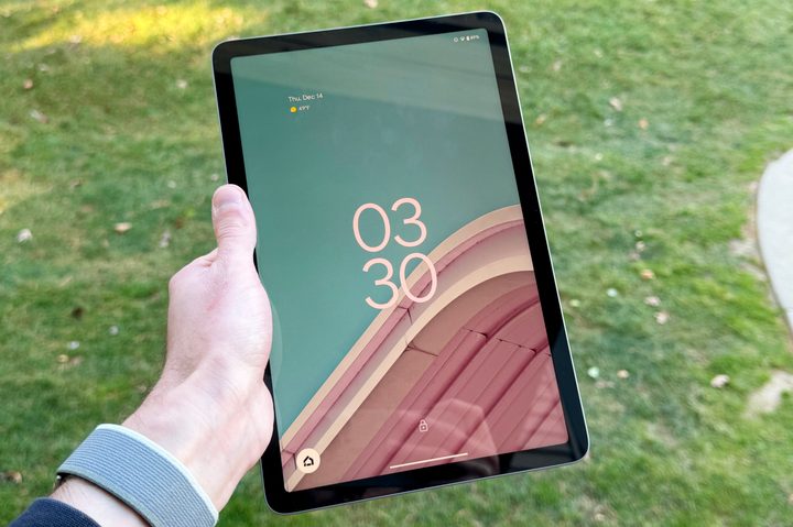Someone holding the Google Pixel Tablet outside. Its screen is turned on.