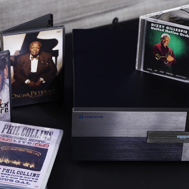 A Magnetar UDP 900 Blu-ray player with a selection of DVDs and audio CDs around it.