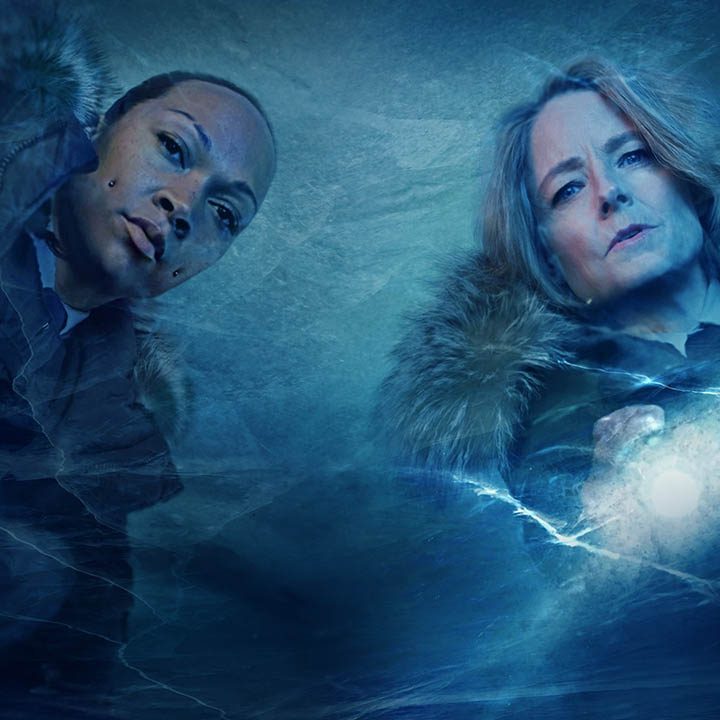 Two women stand over ice and look.