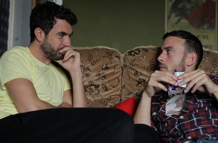 Two men talk to each other on a couch in Weekend.