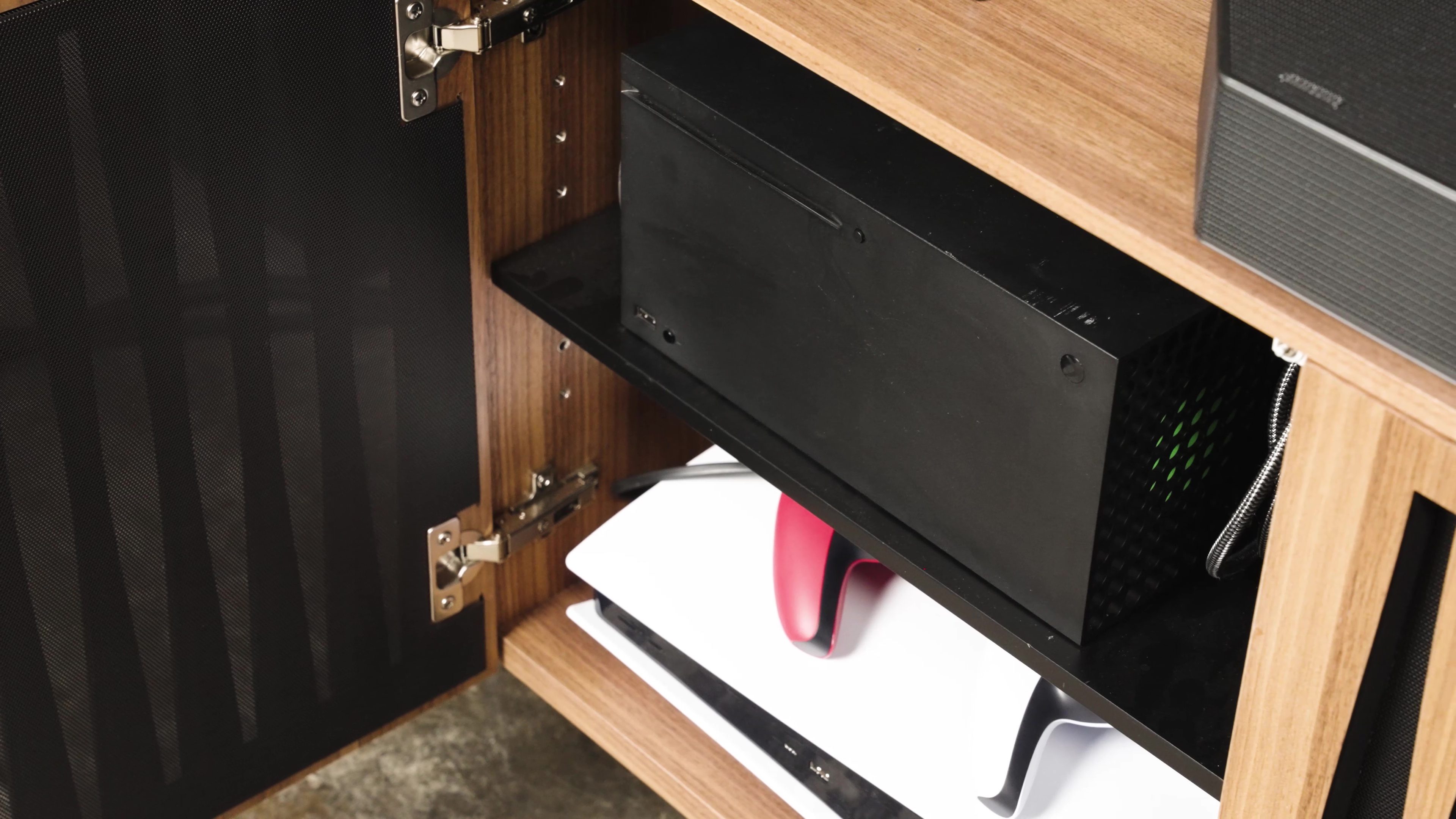 Xbox Series X and a PS5 on the shelves of a media cabinet.