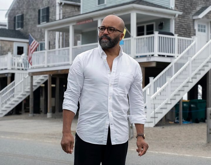A man stands and stares on a road outside a house.