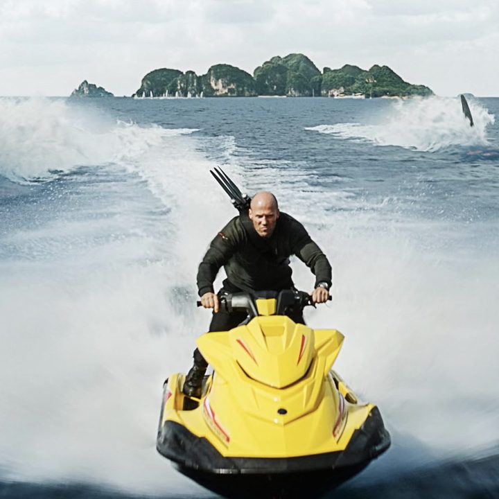 A man rides a jet ski in front of two sharks.