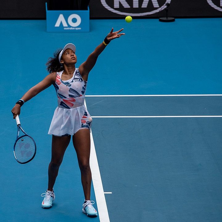 Naomi Osaka throws a tennis ball in the air.