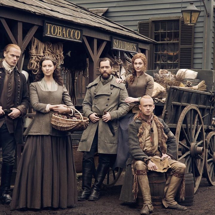 Five people pose in front of a store in the 1700s.