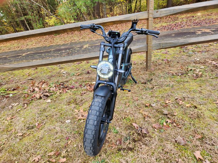 Ride1Up Revv1 left front view with headlamp onb on kickstand in front of a rail fence.