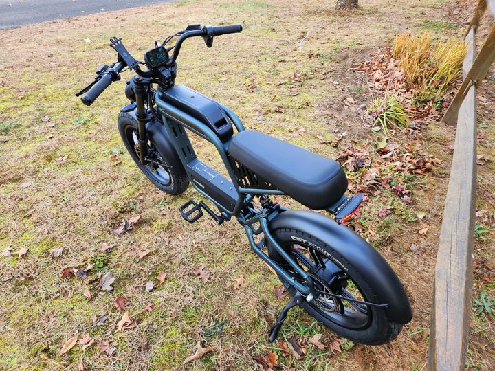 Ride1Up Revv1 left rear three-quarter view parked on grass next to a wooden rail fence.