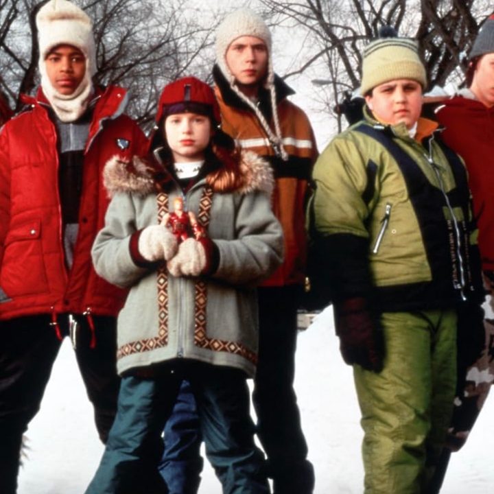 A group of teens in snow gear stand in the snow.