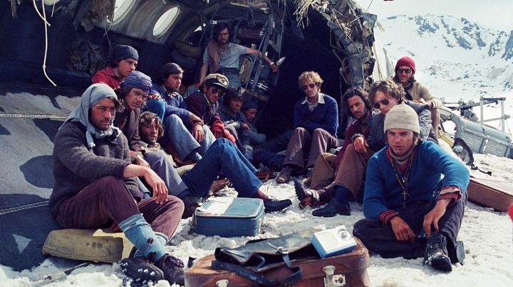 The survivors huddle around in the wreckage of the plane in a still from Society of the Snow