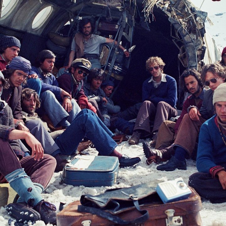 The survivors huddle around in the wreckage of the plane in a still from Society of the Snow