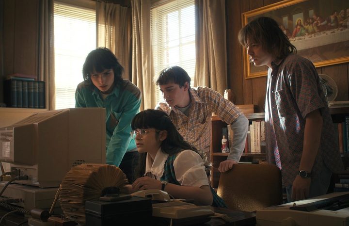 Four kids gather around a desk and stare at the computer.