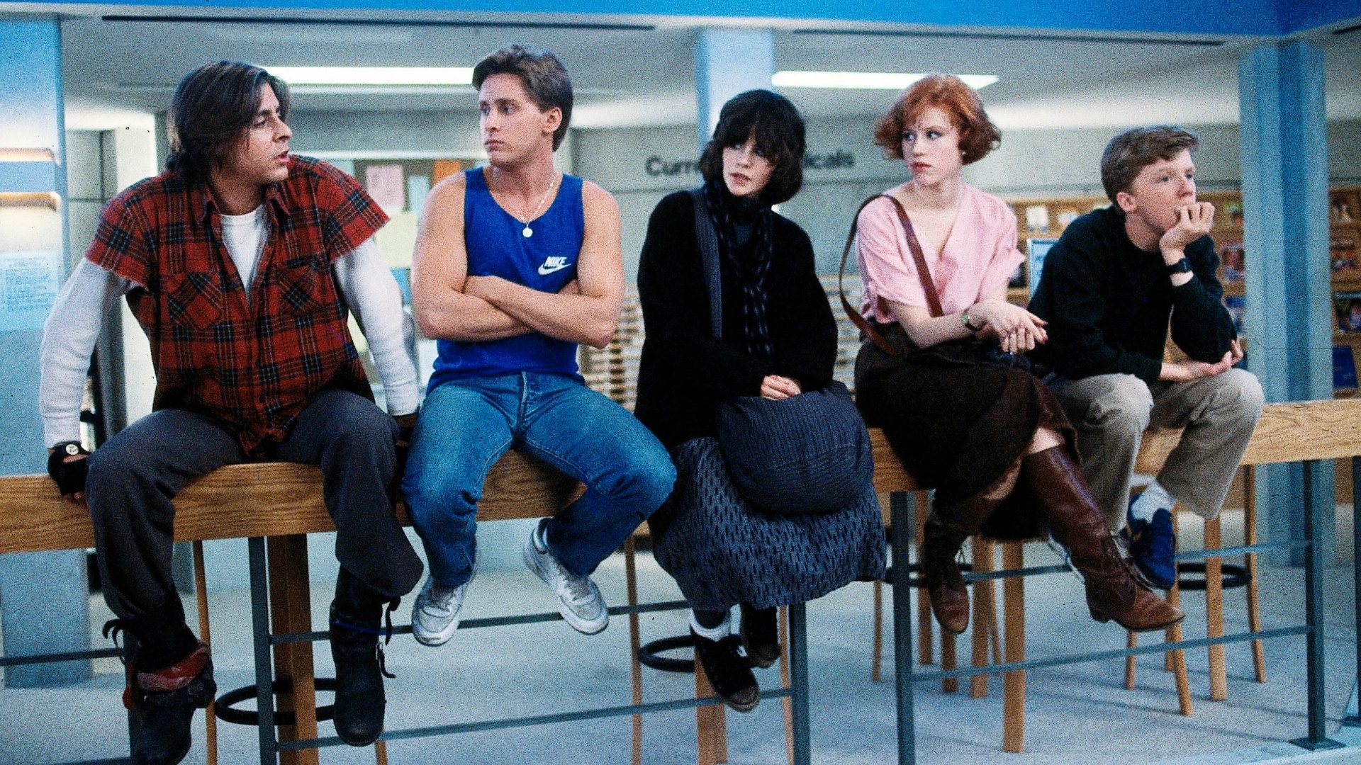 The cast of The Breakfast Club sits in a line of chairs in a still from the 1985 movie.