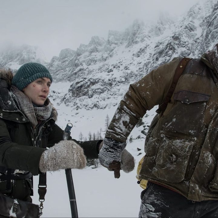 A man and woman walks through the snow in a mountain.