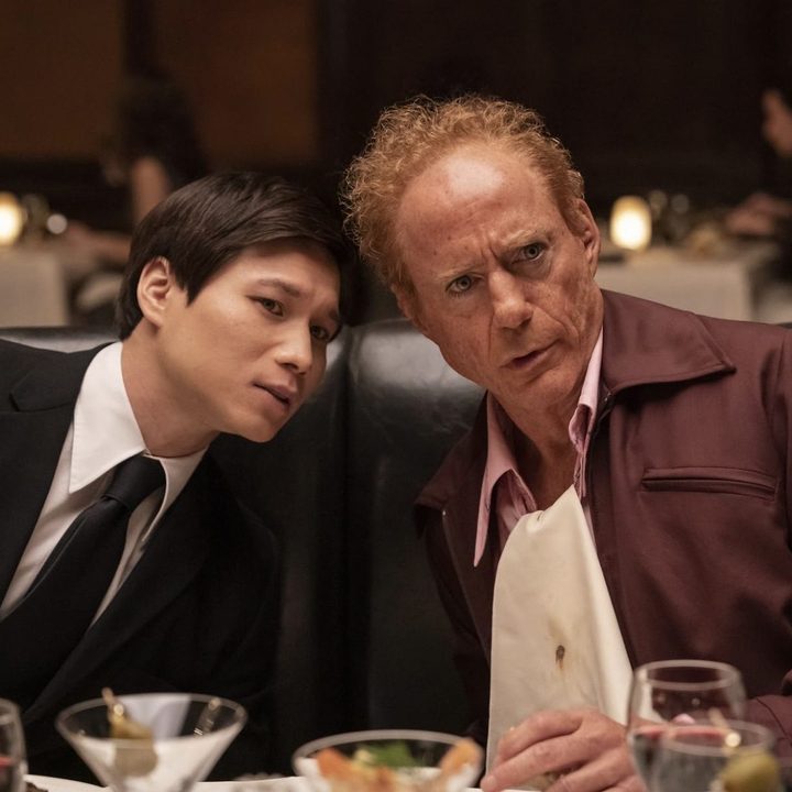 Two men sit at a table next to each other in The Sympathizer.