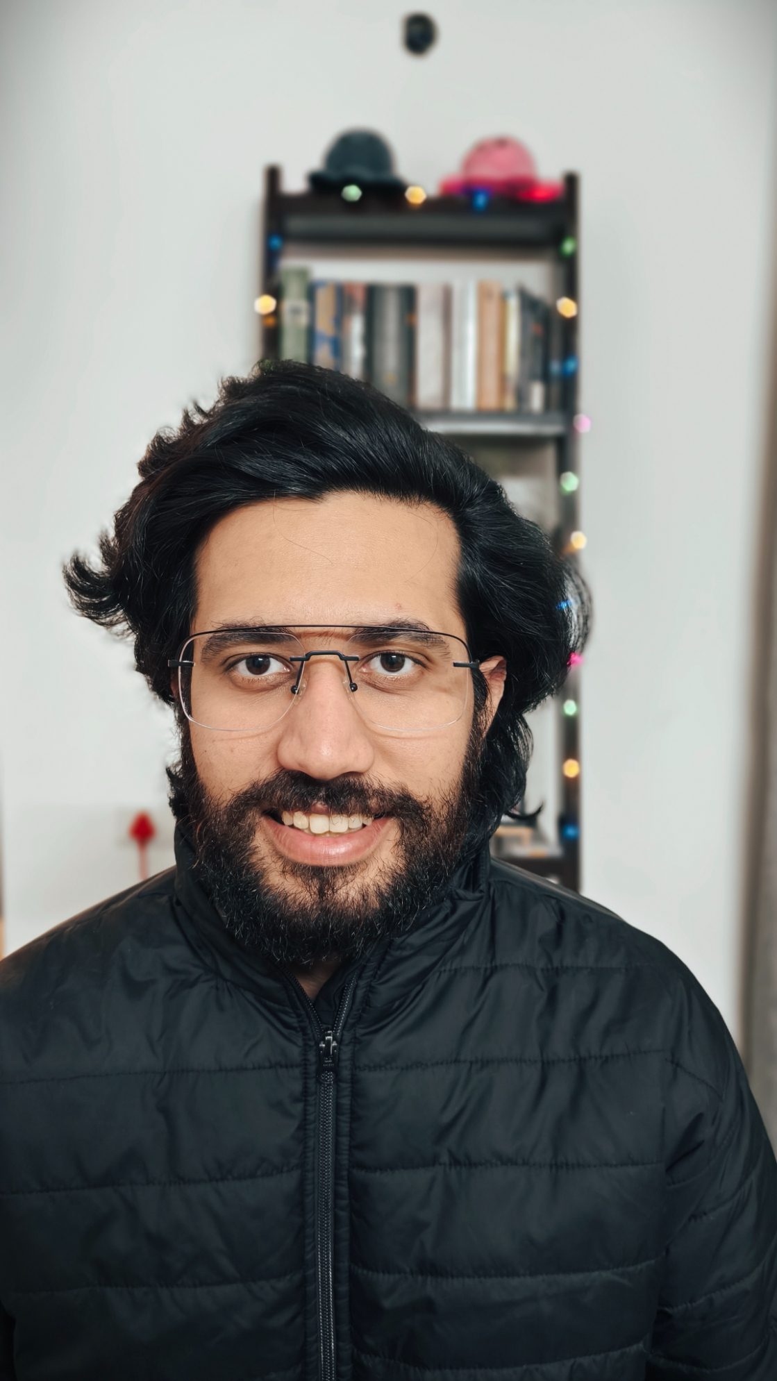 Portrait of a man in black bomber jacket in front of a book rack with fairy lights shot on the Vivo X100 Zeiss camera.