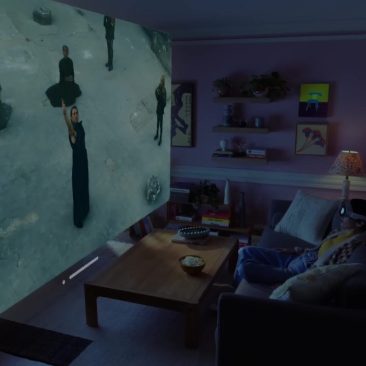 A man sits on a couch wearing an Apple Vision Pro using it as a home theater device.