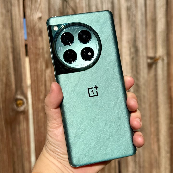OnePlus 12 in Flowy Emerald held in hand in sunlight.